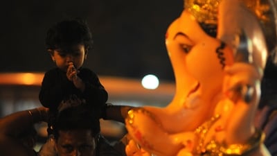 A young devotee sits on the shoulders of a man as he joins hands and closes eyes in front of Lord Ganesh ahead of Ganesh Chatuthi celebrations in Pune. (Mahendra Kolhe/Hindustan Times)