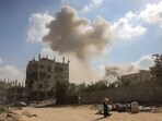 A Palestinian woman walks past personal belongings as smoke billows following an explosion in the Saftawi neighbourhood, west of Jabalia in the Gaza Strip on August 25, 2025.