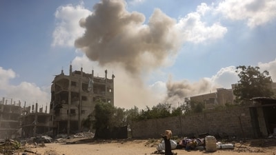 A Palestinian woman walks past personal belongings as smoke billows following an explosion in the Saftawi neighbourhood, west of Jabalia in the Gaza Strip on August 25, 2025. (AFP) A Palestinian woman walks past personal belongings as smoke billows following an explosion in the Saftawi neighbourhood, west of Jabalia in the Gaza Strip on August 25, 2025. (AFP)