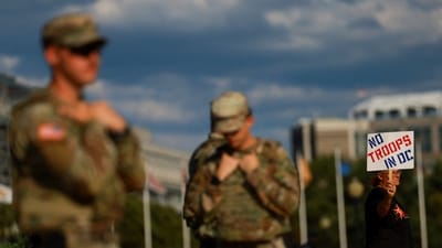 A person holds a protest sign as members of the Louisiana National Guard patrol Union Station weeks after US President Donald Trump ordered National Guard and law enforcement to patrol the nation’s capital to assist in crime prevention, in Washington, DC, on August 25, 2025. (REUTERS)