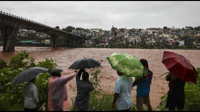 People near the Tawi river that is in spate amid rainfall in Jammu on Tuesday. The river has crossed the 20-ft danger mark in Udhampur district, while downstream in Jammu it is flowing below the alert level, officials said. (PTI Photo)
