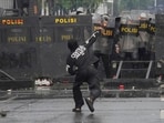 Police officers cover themselves with riot shields as a protester throws rock at them during a protest against lavish allowances given to parliament members, outside the parliament in Jakarta, Indonesia, Sunday, Aug. 31, 2025.