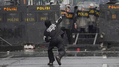 Police officers cover themselves with riot shields as a protester throws rock at them during a protest against lavish allowances given to parliament members, outside the parliament in Jakarta, Indonesia, Sunday, Aug. 31, 2025. (AP)
