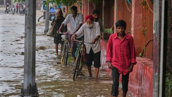 Pedestrians are seen wading though a flooded road after Yamuna overflowed in Delhi following heavy rain.(Manish Swarup/AP)