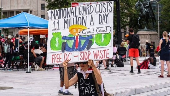 A demonstrator holds a sign calling out Trump for wasting millions on the deployment of National Guard in Washington(Bloomberg)