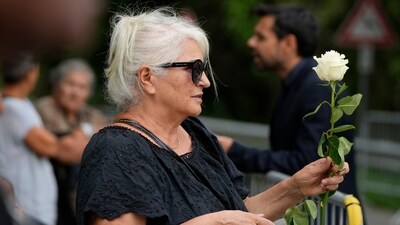 A woman clutches a white rose in quiet anticipation as the hearse carrying the late fashion designer arrives for his funeral. (AP Photo/Luca Bruno) (AP)