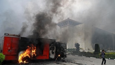 A woman walks past a burning vehicle, set ablaze by protesters inside the premises of the Parliament House in Kathmandu on September 9, 2025, a day after demonstrations over social media prohibitions and corruption by the government. (Prabin Ranabhat/AFP)