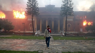 A man is draped in the Nepal national flag as a fire rages through the president's office in Kathmandu on September 9, 2025. (Prabin Ranabhat/AFP)