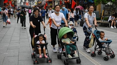 People push baby strollers along a business street in Beijing on July 13, 2021 (AFP FILE)