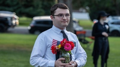 A man wearing a Church of Jesus Christ of Latter-day Saints missionary name tag holds flowers and a US flag during a candlelight vigil for right-wing activist Charlie Kirk at a makeshift memorial at Memorial Park in Provo, Utah, on September 12, 2025, after he was shot during a public event at Utah Valley University.. (Photo by Melissa MAJCHRZAK / AFP) (AFP) A man wearing a Church of Jesus Christ of Latter-day Saints missionary name tag holds flowers and a US flag during a candlelight vigil for right-wing activist Charlie Kirk at a makeshift memorial at Memorial Park in Provo, Utah, on September 12, 2025, after he was shot during a public event at Utah Valley University.. (Photo by Melissa MAJCHRZAK / AFP) (AFP)