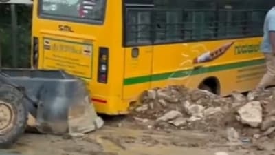 In the video released by PTI, a JCB machine is seen trying to push the bus out of the stormwater drain, while residents overlook the efforts. (X Video grab/@PTI_News) In the video released by PTI, a JCB machine is seen trying to push the bus out of the stormwater drain, while residents overlook the efforts. (X Video grab/@PTI_News)