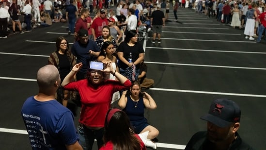 Attendees play a game while waiting in line to enter a memorial service for Turning Point USA founder Charlie Kirk at State Farm Stadium in Glendale, Arizona, US, on Sunday, Sept. 21, 2025.&nbsp;(Bloomberg)