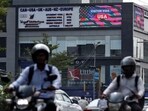 Men riding motorbikes travel past an advertisement of a visa consultancy office in Ahmedabad