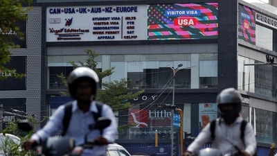 Men riding motorbikes travel past an advertisement of a visa consultancy office in Ahmedabad (REUTERS)