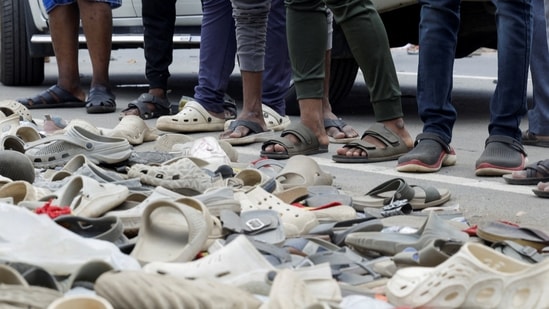 People stand next to the pile of footwear left by people who participated in an election campaign rally held by Tamilaga Vettri Kazhagam party, at the site of a stampede incident, in Karur district of Tamil Nadu(Priyanshu Singh/Reuters)