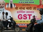 Commuters ride past a new Goods and Services Tax (GST) banner in Varanasi on September 24 (AFP)