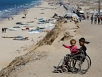 Displaced Palestinian children sit in a wheelchair by the side of a road, after Hamas agreed to release hostages and accept some other terms in a US plan to end the war, in the central Gaza Strip on October 4, 2025.