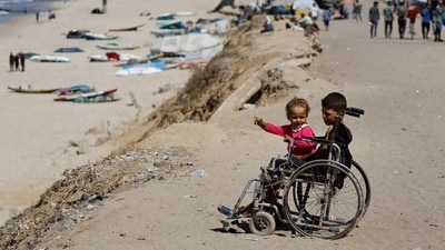 Displaced Palestinian children sit in a wheelchair by the side of a road, after Hamas agreed to release hostages and accept some other terms in a US plan to end the war, in the central Gaza Strip on October 4, 2025. (Mahmoud Issa/Reuters)