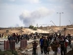 A plume of smoke rises in the background as Palestinians return from a food distribution point near the Netsarim corridor in the central Gaza Strip. A plume of smoke rises in the background as Palestinians return from a food distribution point near the Netsarim corridor in the central Gaza Strip.