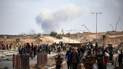 A plume of smoke rises in the background as Palestinians return from a food distribution point near the Netsarim corridor in the central Gaza Strip. (Eyad Baba/AFP) A plume of smoke rises in the background as Palestinians return from a food distribution point near the Netsarim corridor in the central Gaza Strip. (Eyad Baba/AFP)