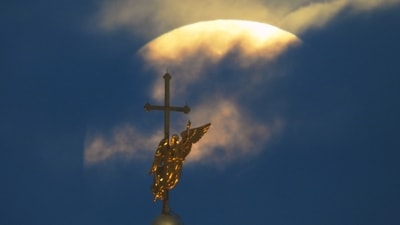 The Harvest Supermoon sets in the clouds behind the city landmark, a weather vane in the form of an angel fixed atop a spire of the Saints Peter and Paul Cathedral in St. Petersburg, Russia on October 7, 2025. (AP)