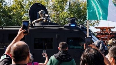 An ICE officer watches protestors as a Lenco BearCat vehicle drives to the scene in the Brighton Park neighborhood of Chicago. (AP) An ICE officer watches protestors as a Lenco BearCat vehicle drives to the scene in the Brighton Park neighborhood of Chicago. (AP)