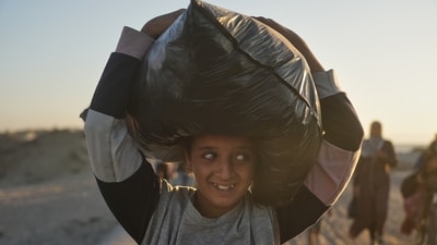 A displaced Palestinian girl carries a bag on her head and walks along the coastal road as she heads back home in Gaza after Israel and Hamas agreed to a pause in their war and the release of the remaining hostages. (Abdel Kareem Hana/AP)