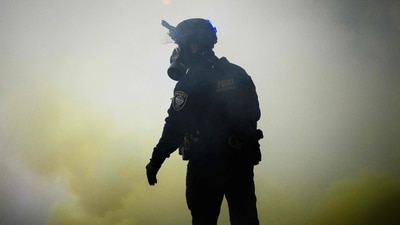 A federal police official stands amid dense smoke as anti ICE protestors clashed with federal forces on October 18, 2025. (Mathieu Lewis-Rolland/Getty Images via AFP)