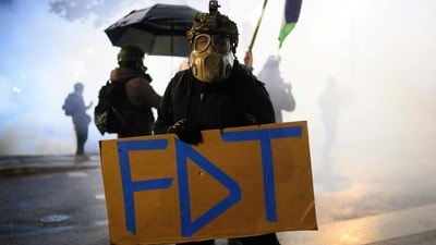 An anti-ICE protester holds a sign in a cloud of tear gas near the US Immigration and Customs Enforcement building on October 18, 2025 in Portland, Oregon. (Mathieu Lewis-Rolland/Getty Images via AFP)