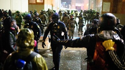 Federal guards stand at the immigration office as protestors approach. (Mathieu Lewis-Rolland/Getty Images via AFP)