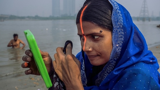 A woman looks at herself in a small mirror amid the Chhath Puja festivities, at a ghat at Kalindi Kunj, in New Delhi.(PTI )