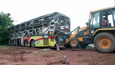 A JCB pulling charred remains of a bus caught fire following a collision with a two-wheeler near the Chinnatekur village, in Kurnool on Friday. (ANI Video Grab) (ANI Video Grab)