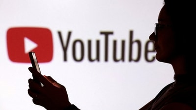 A teenager poses for a photo while holding a smartphone in front of a YouTube logo (REUTERS)