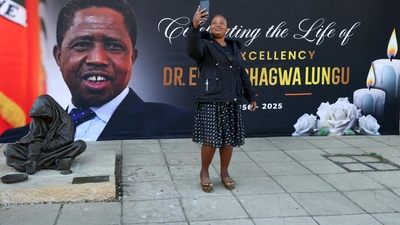 A mourner takes a selfie in front of a banner ahead of the funeral of Edgar Lungu, who died in South Africa in June. A mourner takes a selfie in front of a banner ahead of the funeral of Edgar Lungu, who died in South Africa in June.