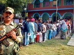 Exit poll results: A security official stands guard as voters wait in queues to cast their votes at a polling booth during the second and final phase of the Bihar assembly elections