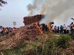 People look on as smoke billows from sugarcane on fire after several tractors and trolleys carrying sugarcane to a factory were allegedly set ablaze by miscreants, in Bagalkote.