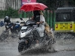 Motorists holding umbrellas ride along a street amid heavy rains in Chennai.