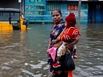 A woman carries a child as she walks past an auto rickshaw partially submerged in water after heavy rains triggered by Cyclone Ditwah in Chennai.
