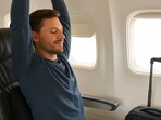 Traveller stretches on a plane, lumbar support in place, luggage nearby, enjoying a journey without back strain or discomfort.(Ai generated)
