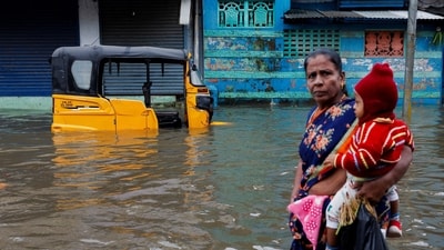 A woman carries a child as she walks past an auto rickshaw partially submerged in water after heavy rains triggered by Cyclone Ditwah in Chennai. (REUTERS)
