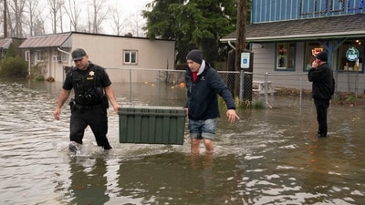 Deputy Sheriff Kalani Apilado helps Brandon Phasith carry belongings while evacuating amidst rising floodwater, as an atmospheric river brings rain and flooding to the Pacific Northwest, in Sultan, Washington, U.S., December 10, 2025.  REUTERS/David Ryder (REUTERS)