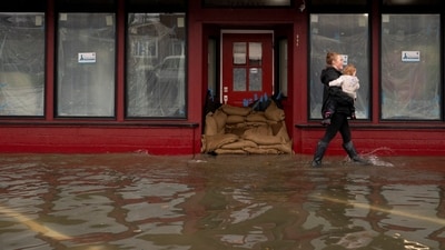 A person carries a child through rising floodwater near a sandbagged business entrance, as an atmospheric river brings rain and flooding to the Pacific Northwest, in Sultan, Washington, U.S., December 10, 2025.  REUTERS/David Ryder (REUTERS)