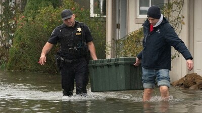 Deputy Sheriff Kalani Apilado helps Brandon Phasith carry belongings while evacuating amidst rising floodwater, as an atmospheric river brings rain and flooding to the Pacific Northwest, in Sultan, Washington, U.S., December 10, 2025.  REUTERS/David Ryder (REUTERS)