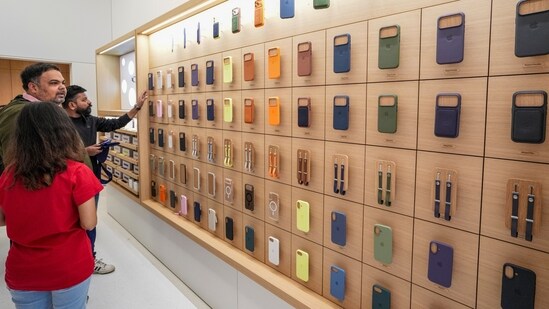 A staff member, in red, assists customers as they check the covers of iPhones during the launch of Apple's new store.(PTI)