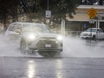 Cars drive through puddles as heavy rain falls due to an atmospheric river, in an intersection in the Woodland Hills area of Los Angeles