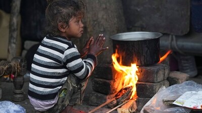 A child sits near a makeshift stove to stay warm on a winter morning in New Delhi. (PTI) A child sits near a makeshift stove to stay warm on a winter morning in New Delhi. (PTI)