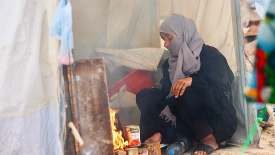 A displaces Palestinian woman cooks food on a fire at a tent amid makeshift shelters as the region experiences cold winter conditions in Al-Mawasi refuge camp in the southern Gaza Strip on December 29, 2025.(AFP)