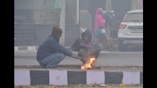 People sit around a bonfire to warm themselves amid dense fog on a cold winter morning in Amritsar on Tuesday. (Sameer Sehgal/HT)