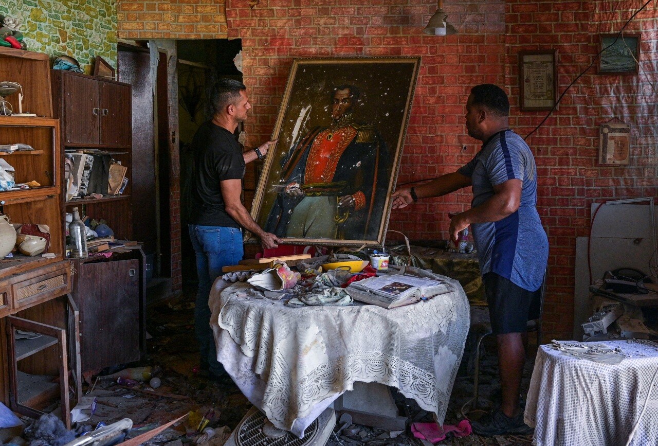 Two men carried a painting of South American independence leader Simón Bolívar at a damaged apartment in Catia La Mar, Venezuela, on Sunday. Two men carried a painting of South American independence leader Simón Bolívar at a damaged apartment in Catia La Mar, Venezuela, on Sunday.