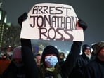 A protester holds a sign reading "ARREST JONATHAN ROSS" during a rally for Renee Good, Jan. 8, 2026, in Minneapolis, after she was fatally shot the day before. 
